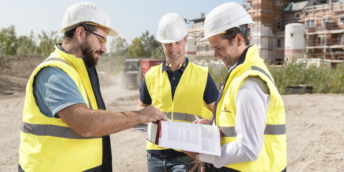 Three building professionals at construction site looking at documents