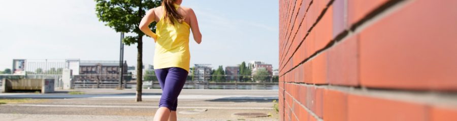 Frog perspective of female jogger next to redish brick facade