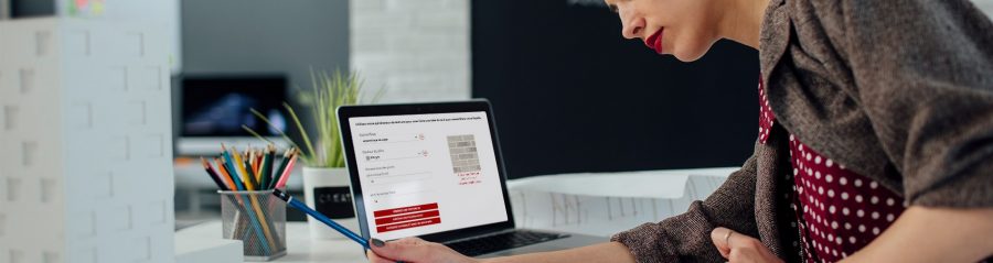 Female architect working in her new modern office. Standing and examining blueprints for her new project. There are on the desk in front of her laptop, architectural model on new business building and color swatch.