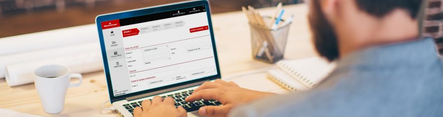 Young man working at modern office space, working on project. Sitting at the table and using laptop. Brick wall in background. Over the shoulder view.