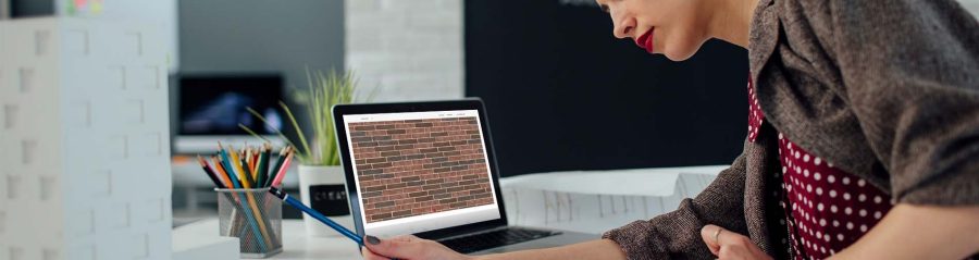 Female architect working in her new modern office. Standing and examining blueprints for her new project. There are on the desk in front of her laptop, architectural model on new business building and color swatch.