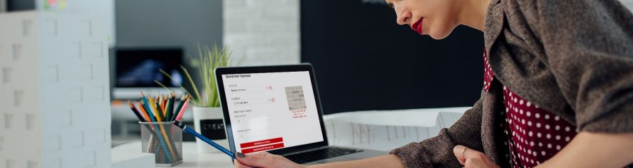 Female architect working in her new modern office. Standing and examining blueprints for her new project. There are on the desk in front of her laptop, architectural model on new business building and color swatch.